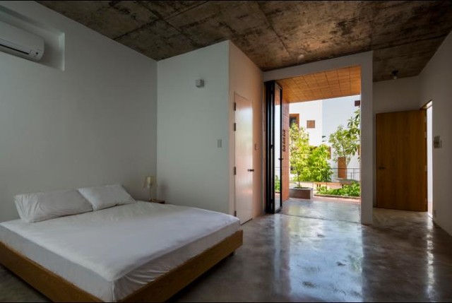 Một phòng ngủ tầng 1 rộng rãi với sàn láng xi măng nhẵn bóng và trần bê tông.